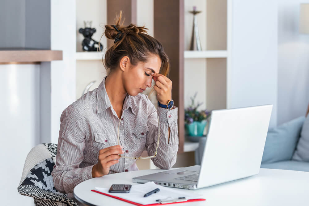 Young woman working in front of laptop suffering from headaches